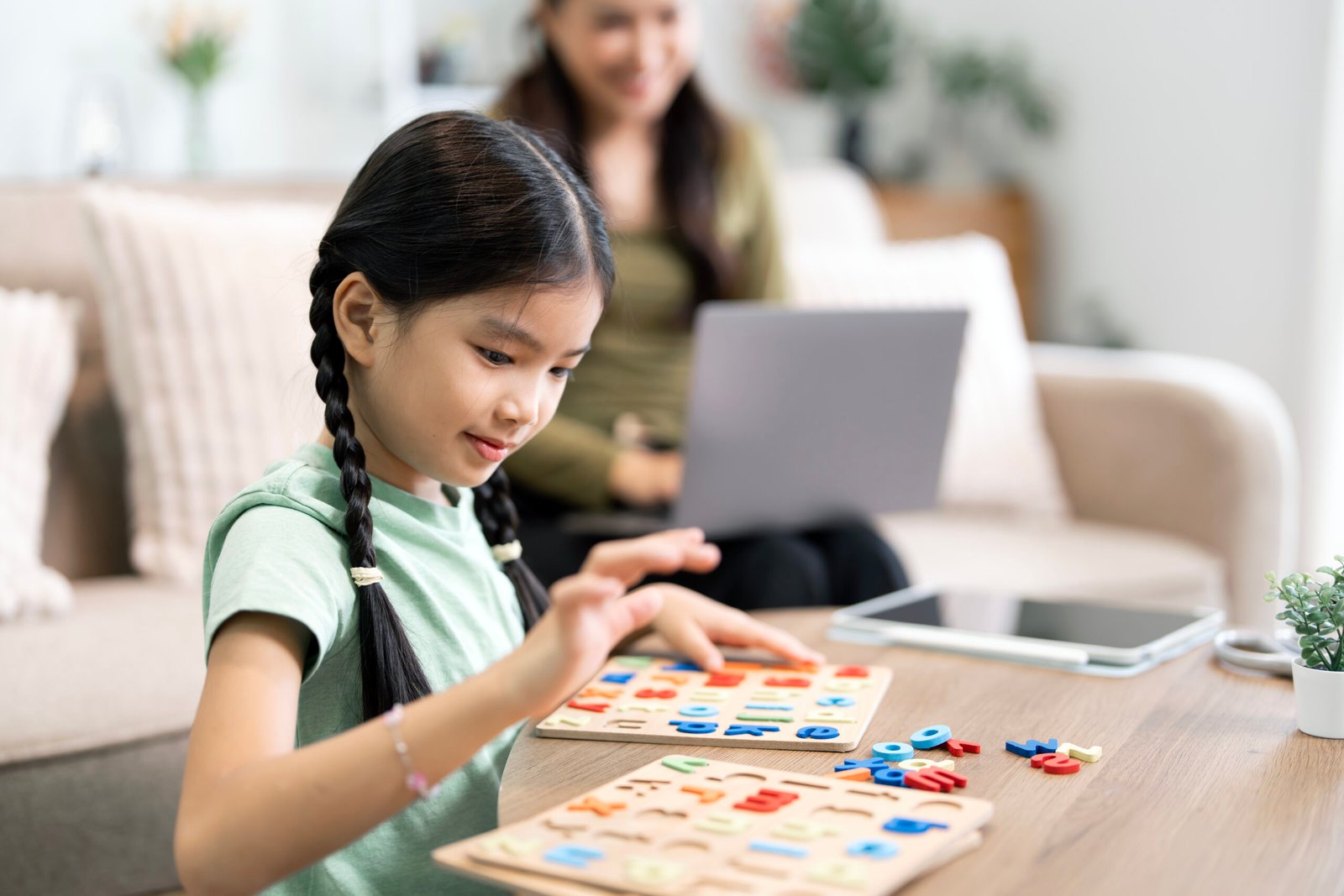 little asian girl playing alphabet puzzle with mother working be